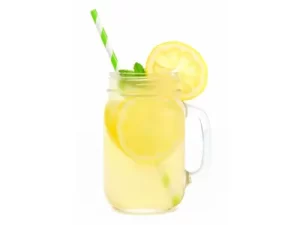 Limonada s slamico v kozarcu z ledom, okrašena s kolutom limone na belem ozadju